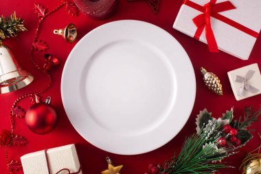 Boş beyaz tabak ve kırmızı arka planda Noel süsü. Noel yemeği konsepti.