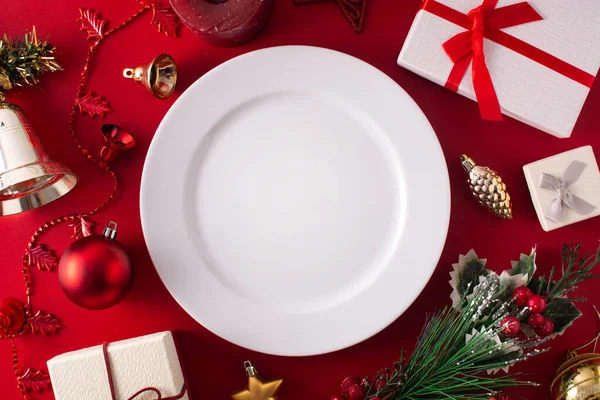 Boş beyaz tabak ve kırmızı arka planda Noel süsü. Noel yemeği konsepti.