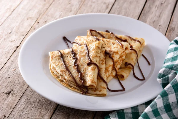 Sweet crepes with chocolate on wooden table