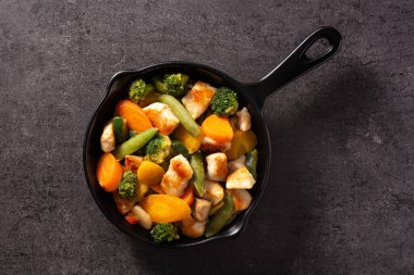 Tavuğu sebzeyle karıştır, siyah arka planda demir tavada.