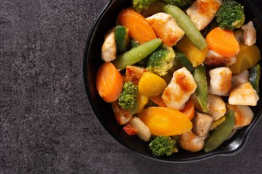 Kızarmış tavuğu siyah arka planda demir tavada sebzeyle karıştır. Üst Manzara. Boşluğu kopyala