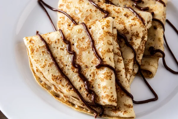 Sweet crepes with chocolate on wooden table.