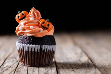 Köylü ahşap masasında balkabağı süslemeli Cadılar Bayramı kekleri ve siyah arka plan. Boşluğu kopyala