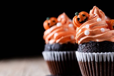 Köylü ahşap masasında balkabağı süslemeli Cadılar Bayramı kekleri ve siyah arka plan. Boşluğu kopyala