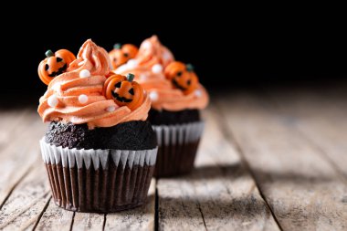 Köylü ahşap masasında balkabağı süslemeli Cadılar Bayramı kekleri ve siyah arka plan. Boşluğu kopyala