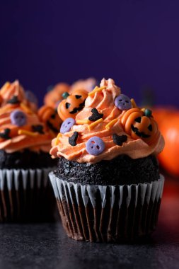 Cadılar Bayramı kekleri, siyah yüzey ve mor arka plan üzerine serpiştirilmiş.