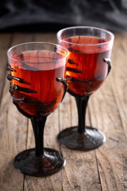 Halloween spooky red cocktail in skeleton hand glass on wooden table