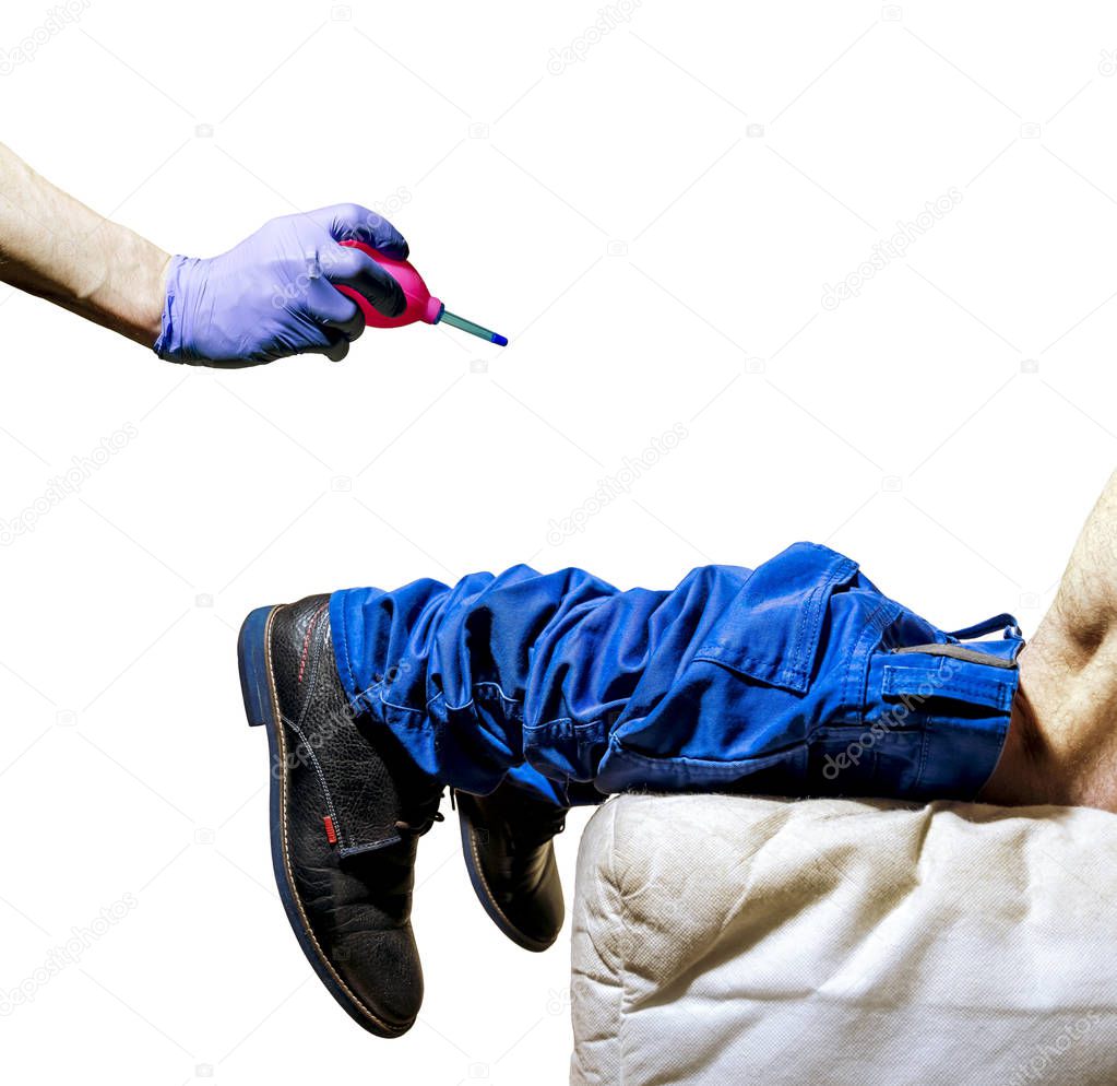 Hand in Glove holds pear-shaped enema in front of man's leg with his trousers down on his knees on the couch isolated on white background