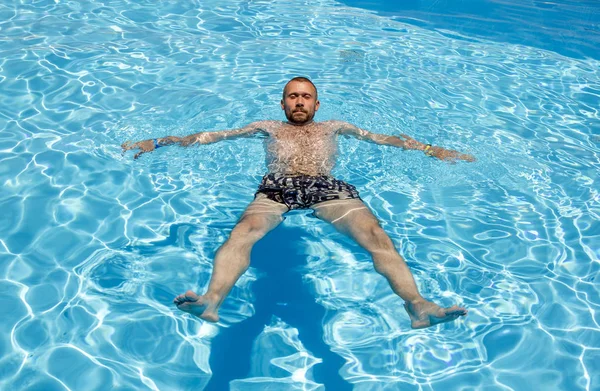 Мужчина плавает в бассейне в яркий солнечный день — стоковое фото