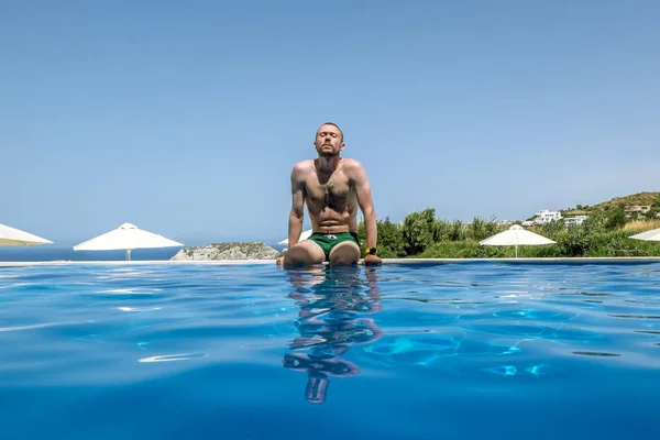 Un hombre toma el sol en el borde de la piscina en un día soleado — Foto de Stock