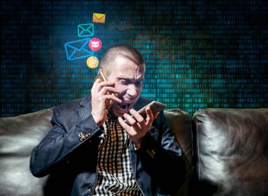 Takım elbiseli bir adam, iki akıllı telefondan matris numaralarının arka planına karşı duygusal olarak konuşur.