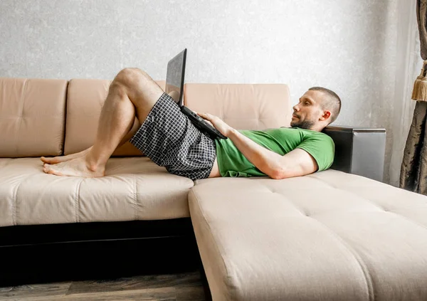 Bir Adam Kanepede Yatarken Internette Dizüstü Bilgisayarla Çalışır Çalışır — Stok fotoğraf