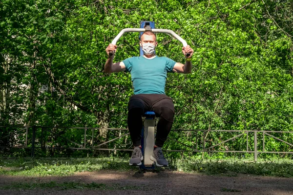 A man in a medical mask trains on sports equipment in a courtyard in the city during the pandemic