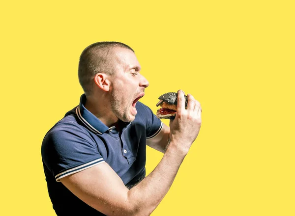 Hombre Hambriento Disfruta Comiendo Una Hamburguesa Negra Sobre Fondo Amarillo —  Fotos de Stock