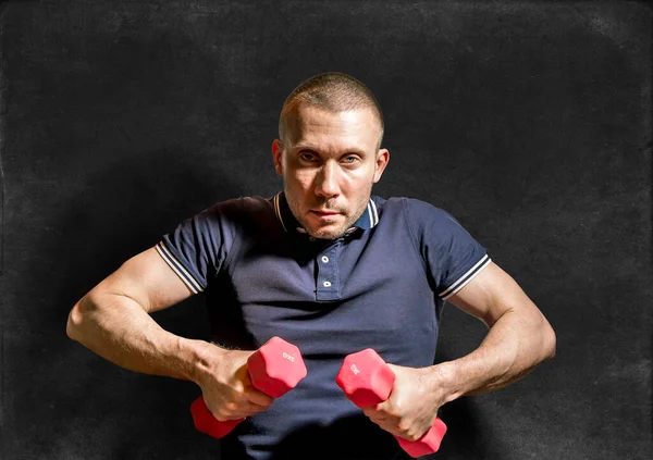 A stern Man holds dumbbells in his hands against the background of a chalkboard.