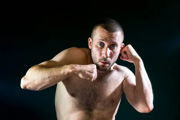 A man in a fighting stance with a naked torso box on a dark background