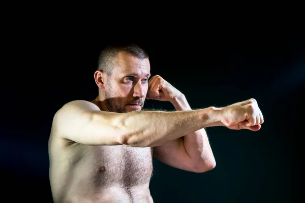 A man in a fighting stance with a naked torso box on a dark background