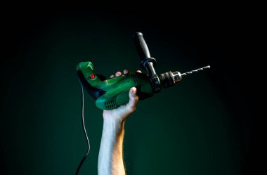 Kalkmış bir erkek eli koyu yeşil bir arka planda matkap tutuyor.