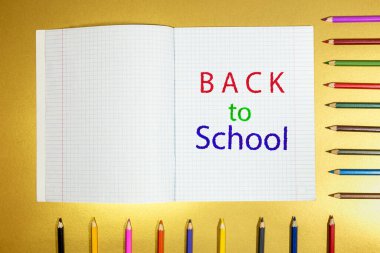 Masanın üzerinde bir defter var. Üzerinde okula dönüş yazısı ve renkli kalemler var..