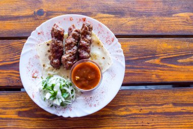 Bir tabakta porsiyonlu luleh kebap. Ahşap masa üzerinde iştah açıcı çanak.