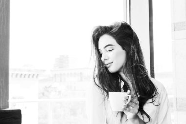 Beyaz gömlekli genç, kahverengi saçlı bir kız kapuçino kahve içiyor.