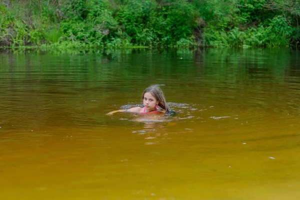 砂の中に座ってピンクの水着で美しい小さなブルネットの女の子 — ストック写真