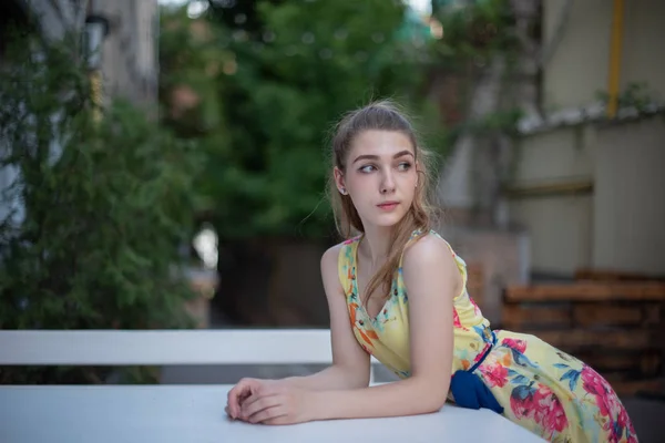 Una joven con largos rizos blancos en un vestido camina por el casco antiguo en el verano. niña en un vestido de flores — Foto de Stock