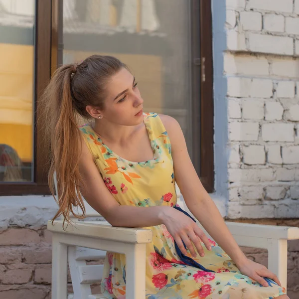 Une jeune fille avec de longues boucles blanches dans une robe se promène dans la vieille ville en été. fille dans une robe de fleurs — Photo