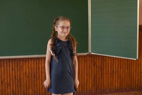 Petite écolière debout au tableau noir. Écolière avec deux nattes dans des lunettes . — Photo