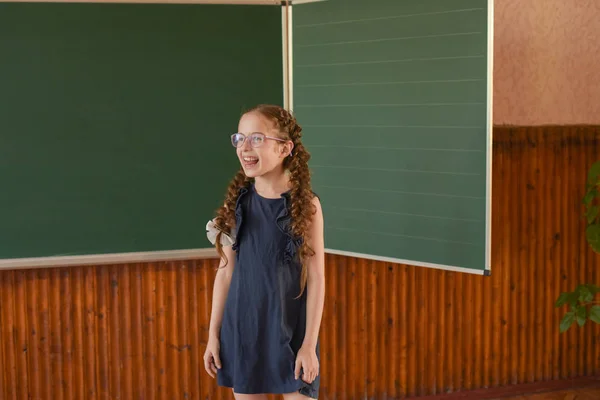 黒板に立つ小さな女子高生眼鏡で2つのピグテールを持つ女子高生. — ストック写真