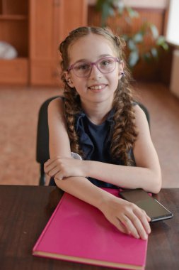 Sınıfta ders kitaplarıyla masada oturan liseli kız. Pigtails ile mavi elbiseli kız.