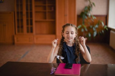 Sınıfta ders kitaplarıyla masada oturan liseli kız. Pigtails ile mavi elbiseli kız.