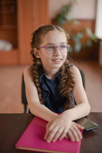 Μαθήτρια που κάθεται στο τραπέζι με σχολικά βιβλία στην τάξη. Κορίτσι σε ένα μπλε φόρεμα με κοτσίδες. — Φωτογραφία Αρχείου