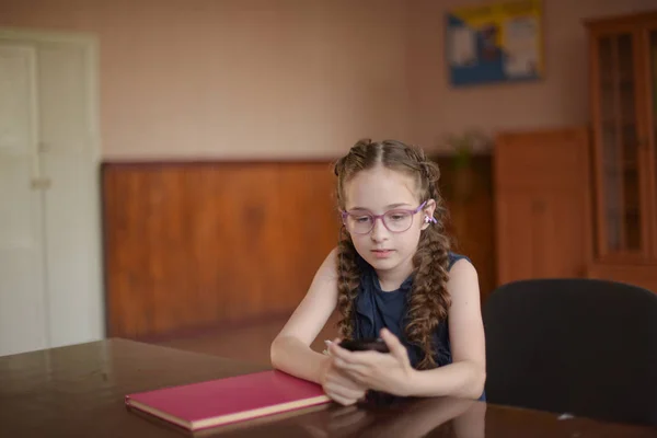 교실에서 교과서와 함께 테이블에 앉아 여학생. 피그 테일과 파란색 드레스를 입은 소녀. — 스톡 사진