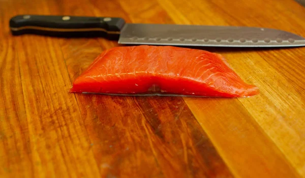 Salmón fresco y cuchillo en tabla de cortar en la mesa de madera. Vista superior . —  Fotos de Stock