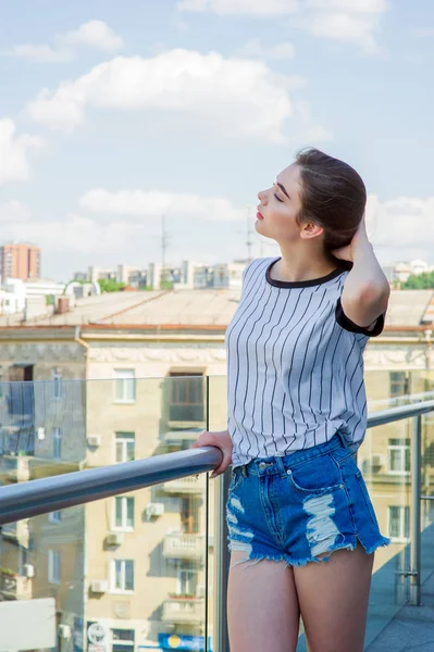 Dziewczynka w szortach na balkonie w kawiarni. Letni Portret młodej stylowej dziewczyny pozując na balkonie, mini szorty dżinsowe — Zdjęcie stockowe