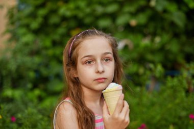 Little girl eat ice cream at an outdoor In a colorful striped bright dress. Sunny summer, hot weather. clipart