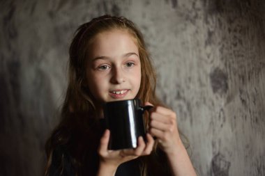 Elinde siyah tişörtlü kahve fincanı tutan küçük bir kız. Tasarımınızı ortaya koymak için mükemmel, alay edin.