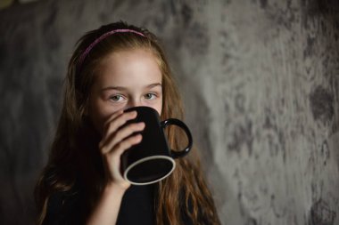 Elinde siyah tişörtlü kahve fincanı tutan küçük bir kız. Tasarımınızı ortaya koymak için mükemmel, alay edin.