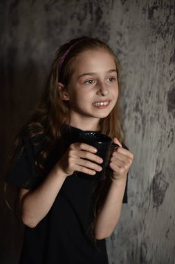 Elinde siyah tişörtlü kahve fincanı tutan küçük bir kız. Tasarımınızı ortaya koymak için mükemmel, alay edin.
