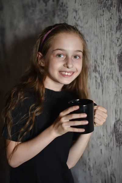 Fetiţa ţine o ceaşcă de cafea în tricou negru. Mock up, perfect pentru a pune designul pe . — Fotografie, imagine de stoc