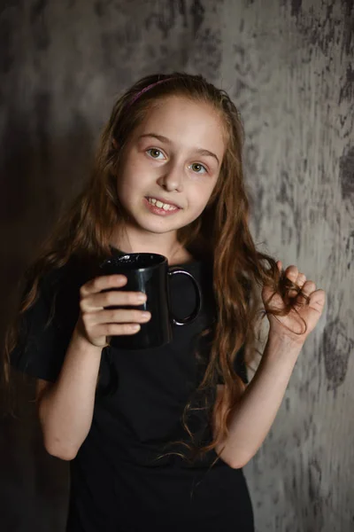 Fetiţa ţine o ceaşcă de cafea în tricou negru. Mock up, perfect pentru a pune designul pe . — Fotografie, imagine de stoc