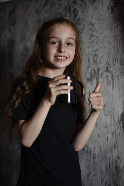Petite fille tenant une tasse de café en t-shirt noir. Maquette, parfait pour mettre votre design sur . — Photo