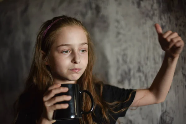 Маленькая девочка держит чашку кофе в черной футболке. Подтянитесь, идеально подходит для размещения вашего дизайна . — стоковое фото