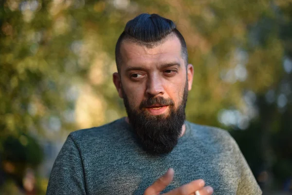 Ein Mann mit Bart raucht in einem grünen T-Shirt in der Natur eine Zigarette — Stockfoto