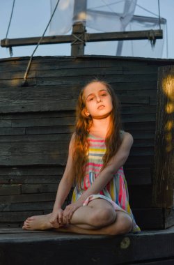 Ahşap güvertede uzun saçlı, bir şey hayal ederken kenara bakan pensive küçük çocuk.