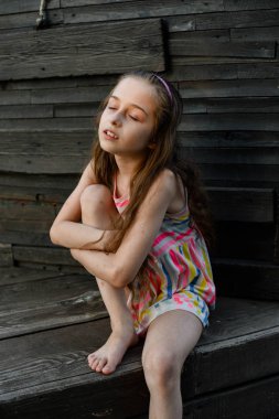 Ahşap güvertede uzun saçlı, bir şey hayal ederken kenara bakan pensive küçük çocuk.
