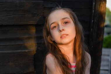 Ahşap güvertede uzun saçlı, bir şey hayal ederken kenara bakan pensive küçük çocuk.