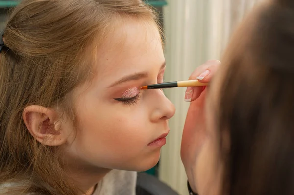 a little girl doing makeup before performing on stage. Preparation before the performance in the dressing room