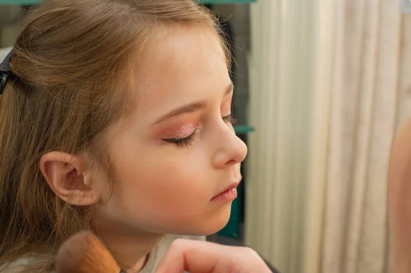 a little girl doing makeup before performing on stage. Preparation before the performance in the dressing room